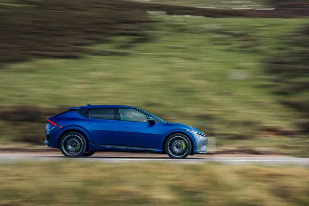 Kia EV6 bleu en mouvement sur route rurale panoramique.