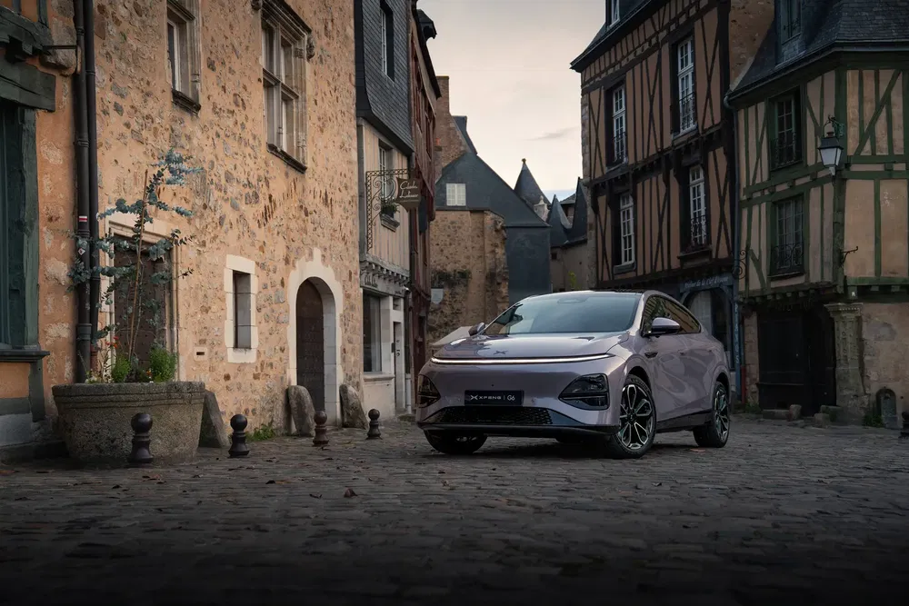 Moderne Xpeng G6 SUV geparkeerd in een schilderachtige Europese dorpsstraat met stenen huizen.