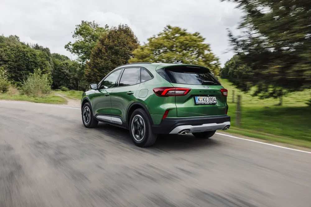Ford Kuga vert roulant sur route de campagne, arbres en arrière-plan.