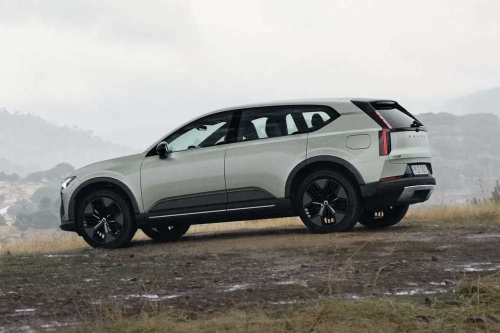 SUV Volvo EX90 blanc sur chemin de terre avec arrière-plan de montagne brumeuse.