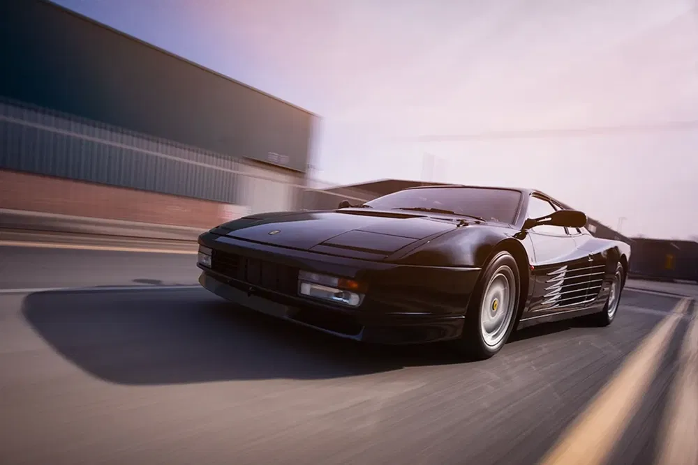 Zwarte Ferrari Testarossa snel rijdend op stedelijke weg, iconisch en stijlvol ontwerp.