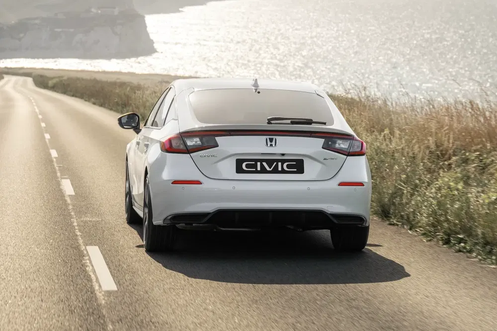 Honda Civic blanche sur une route côtière ensoleillée.