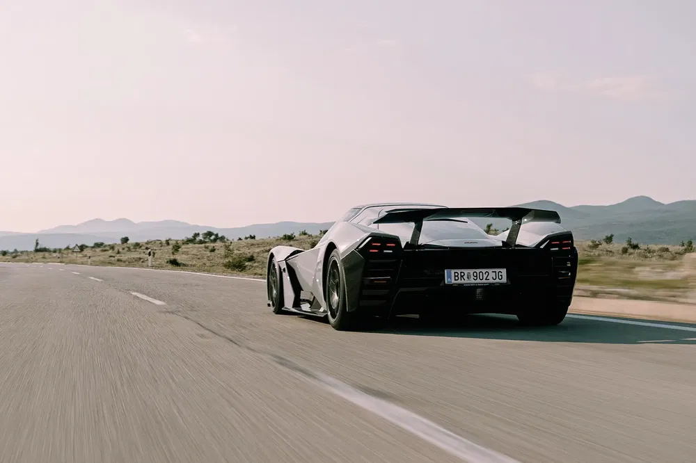 Supercar noire roulant sur autoroute désertique, montagnes en arrière-plan, design aérodynamique.