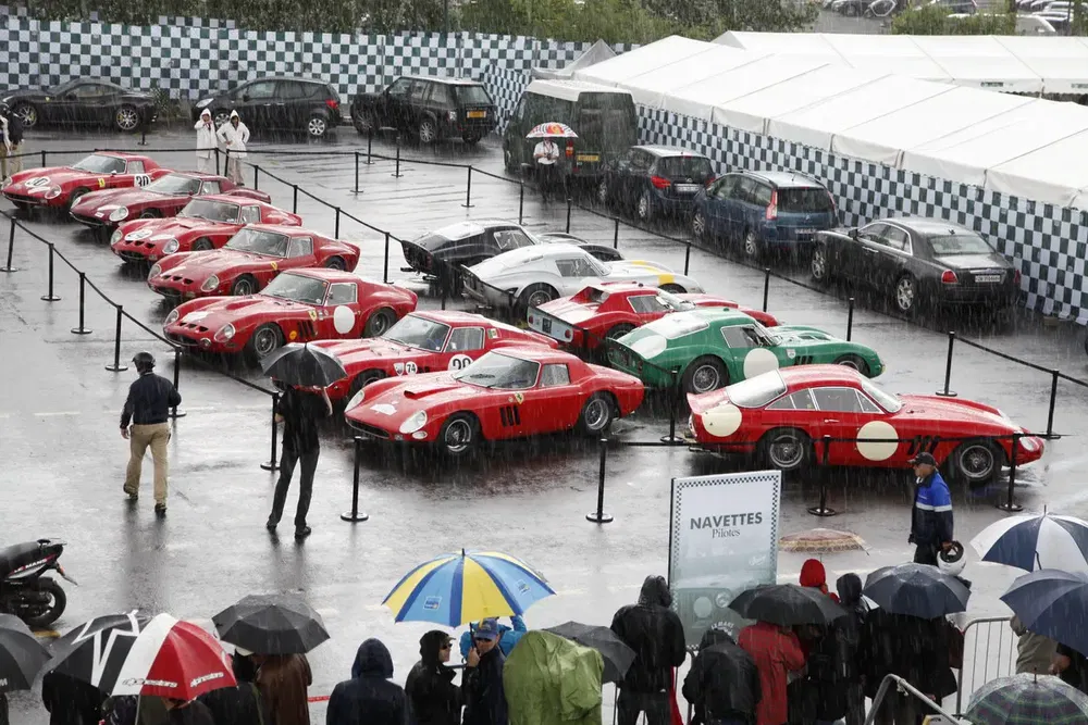 Collection de voitures classiques Ferrari sous la pluie lors d'un événement automobile.