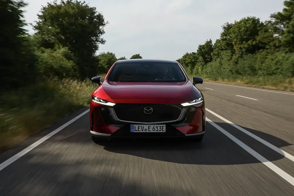 Rode Mazda rijdt op boomrijke weg, Duitse nummerplaat LEV E 613E.