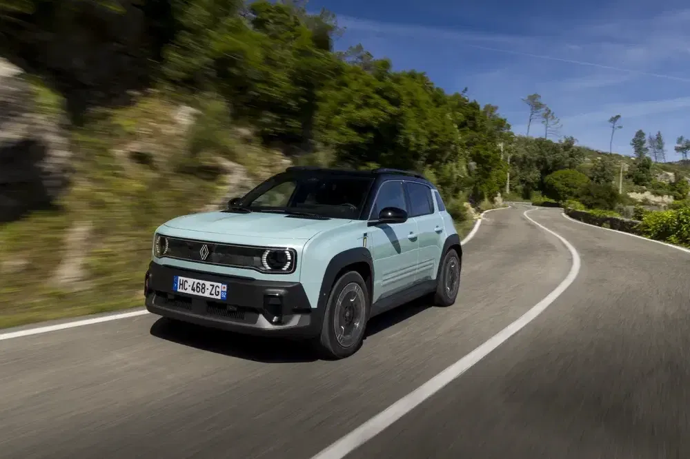 Renault électrique roulant sur route sinueuse entourée d'arbres et de collines verdoyantes.