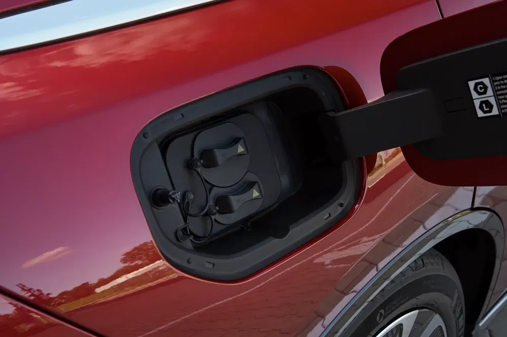 Oplaadpoort op rode auto, wolken weerspiegeld in de carrosserie.