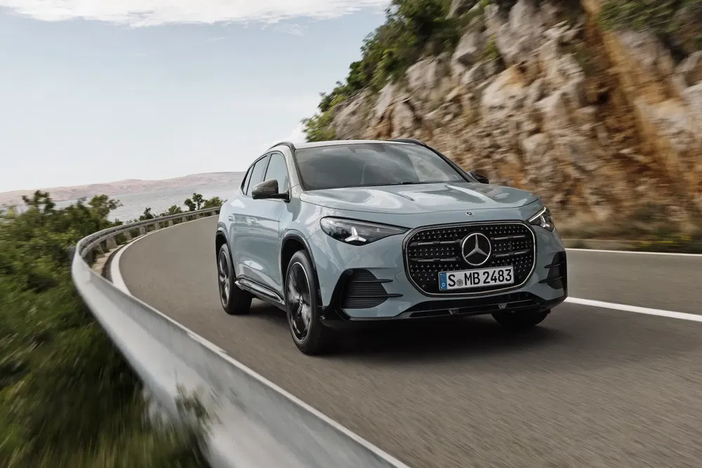 Mercedes-Benz SUV rijdt op een bochtige kustweg, omgeven door rotsachtige en groene landschappen.