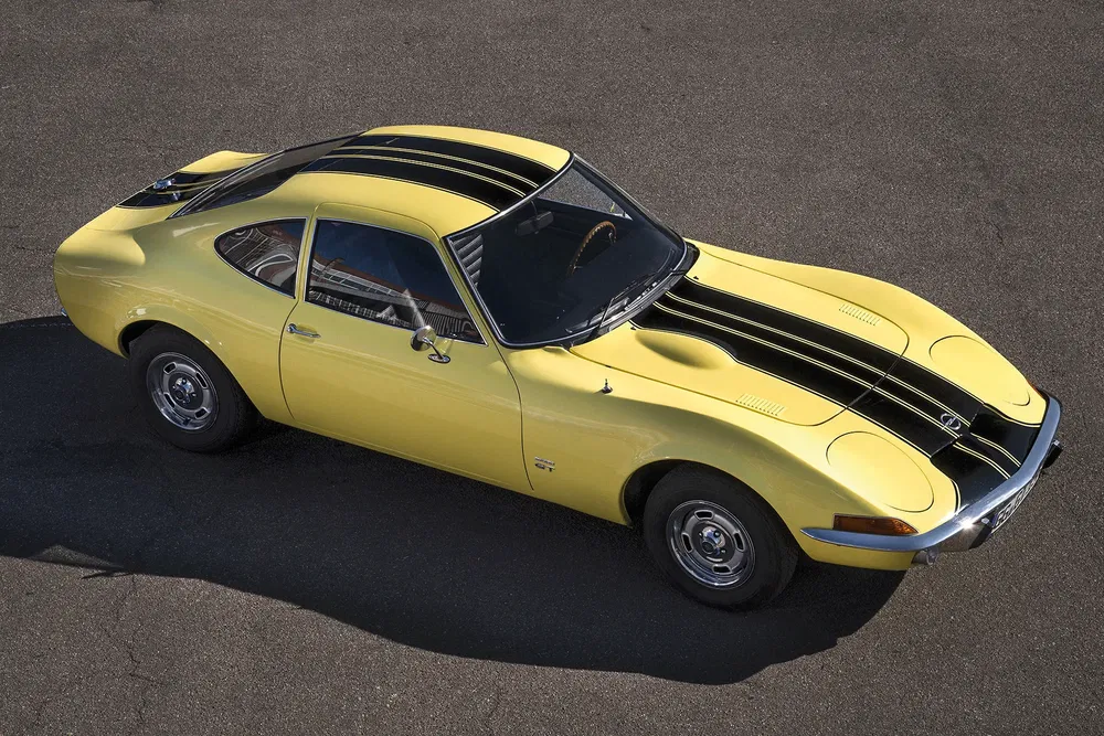 Luchtfoto van een gele Opel GT met zwarte strepen, vintage ontwerp op asfalt.