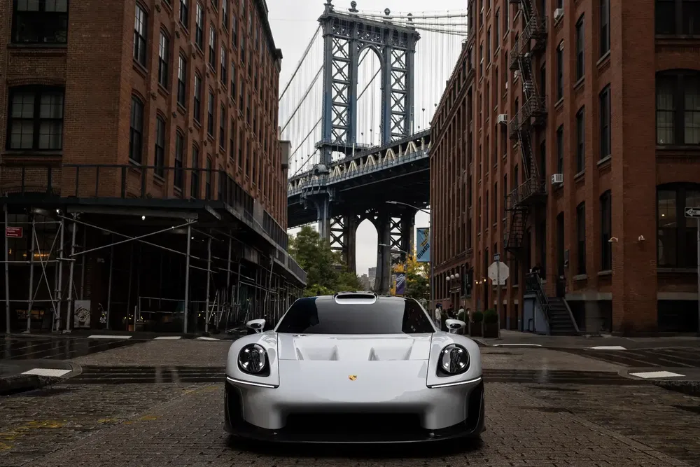 Moderne witte Porsche onder iconische brug, tussen rode bakstenen fabrieksgebouwen.