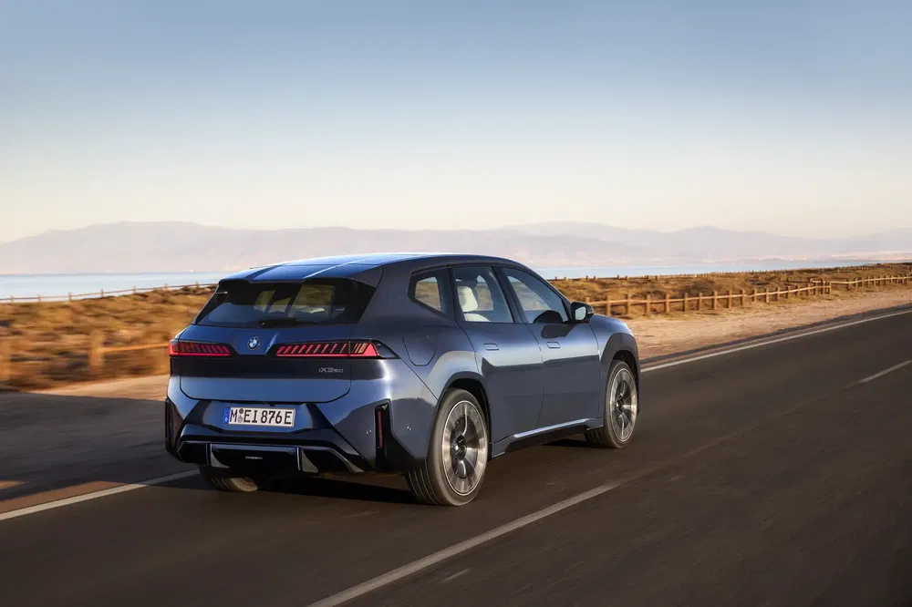 Elektrische BMW iX rijdend op een kustweg met woestijnlandschap.