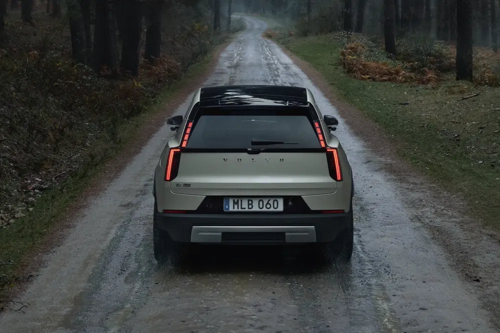 Volvo EX90 sur route forestière humide, vue arrière, design moderne et élégant.