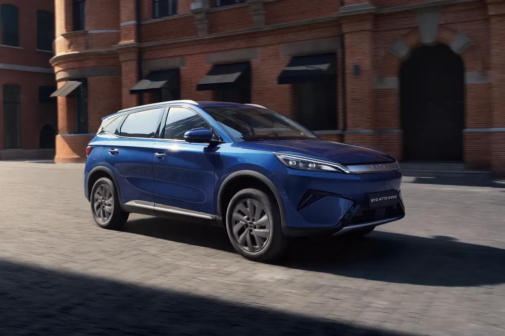 Blauwe BYD Yuan Plus EV rijdt op een geplaveide straat voor een bakstenen gebouw.