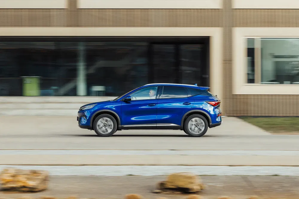 Blauwe BYD Atto 3 rijdt langs een modern gebouw.