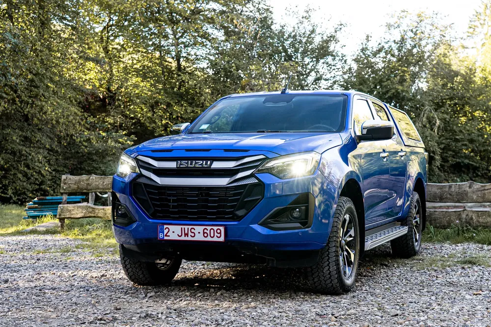 Isuzu D-Max bleu garé en plein air, entouré de verdure et de ciel ensoleillé.