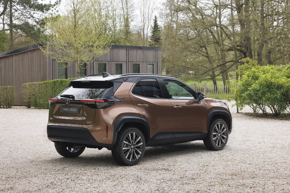 Bruine Toyota Yaris Cross SUV op oprit, stijlvol ontwerp met groene achtergrond.