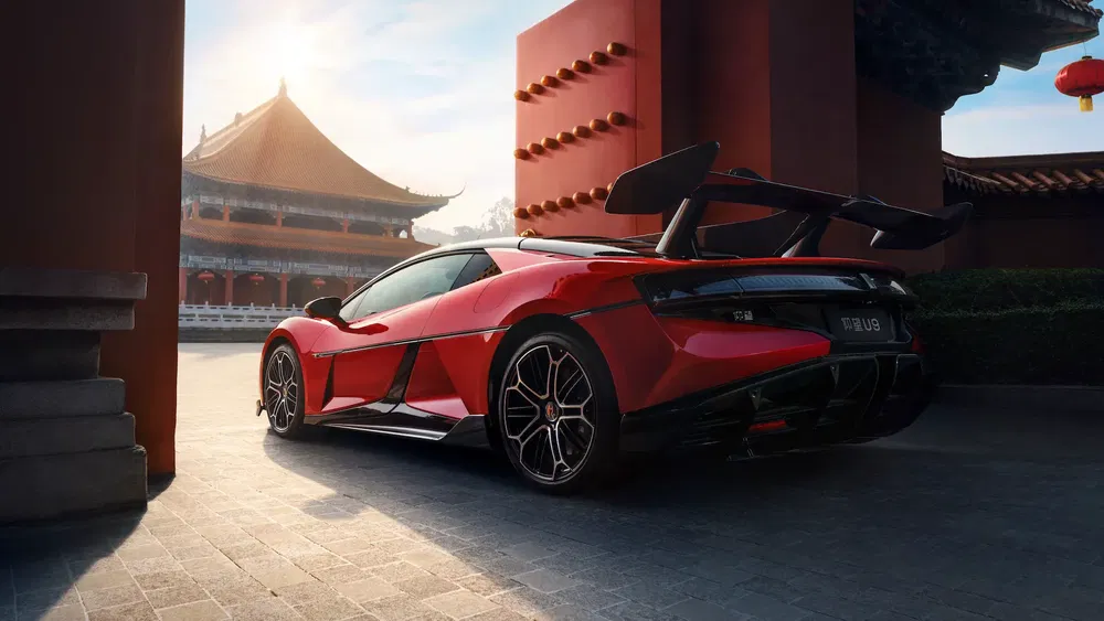Supercar rouge garée devant architecture chinoise traditionnelle, aileron arrière imposant.