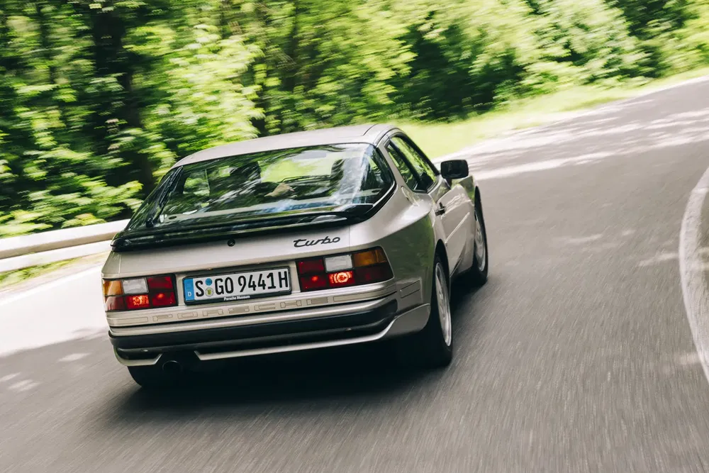 Porsche 944 Turbo argentée sur route sinueuse entourée de verdure luxuriante.