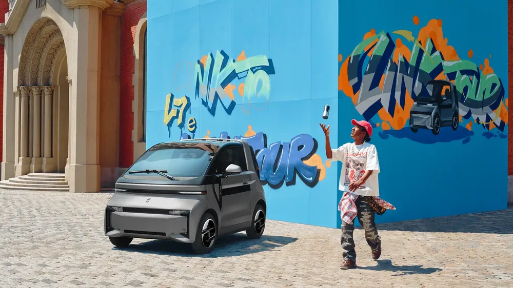 Voiture électrique compacte devant un mur avec des graffitis urbains colorés, jeune prenant une photo.