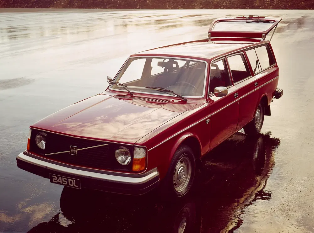 Volvo 245 DL break rouge sur route mouillée, coffre ouvert en arrière-plan.