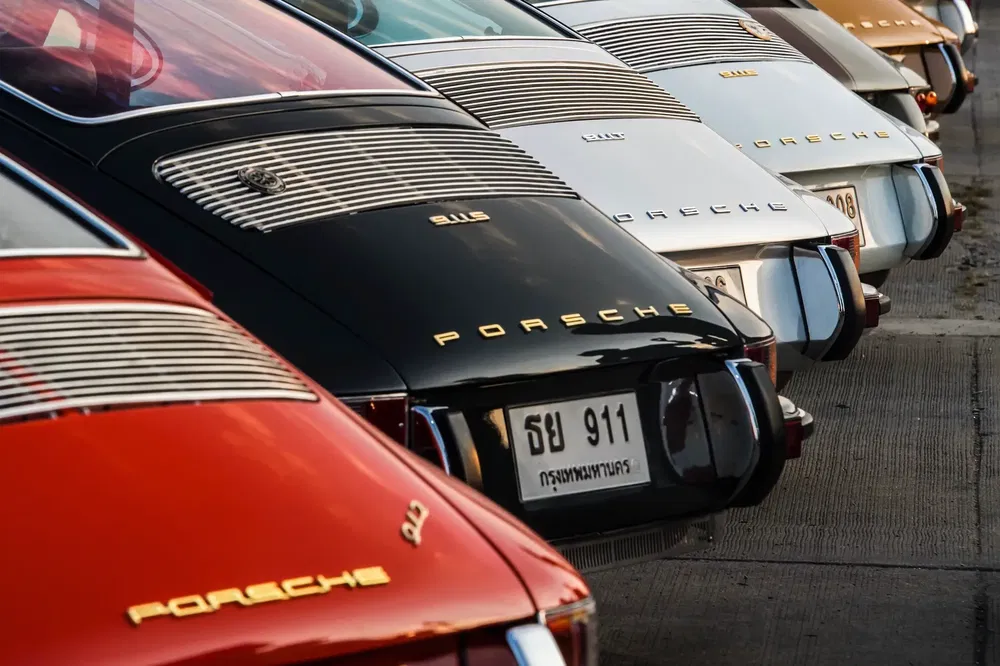 Alignement de Porsche 911 classiques colorées sur un parking, pare-chocs brillants en évidence.
