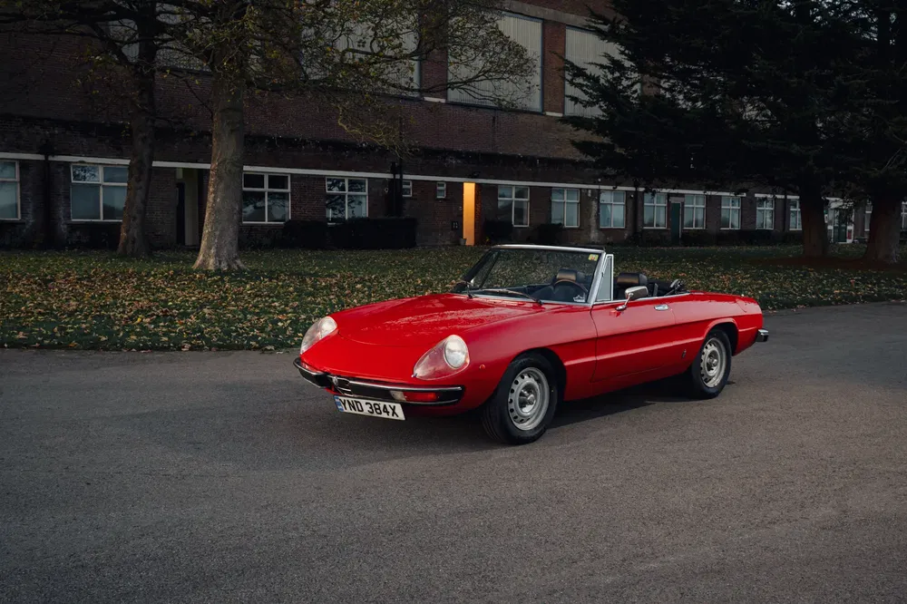 {"fr":"Alfa Romeo Spider rouge décapotable stationnée devant un bâtiment en briques par temps clair.","nl":"Rode Alfa Romeo Spider cabriolet geparkeerd voor een bakstenen gebouw op een heldere dag."}