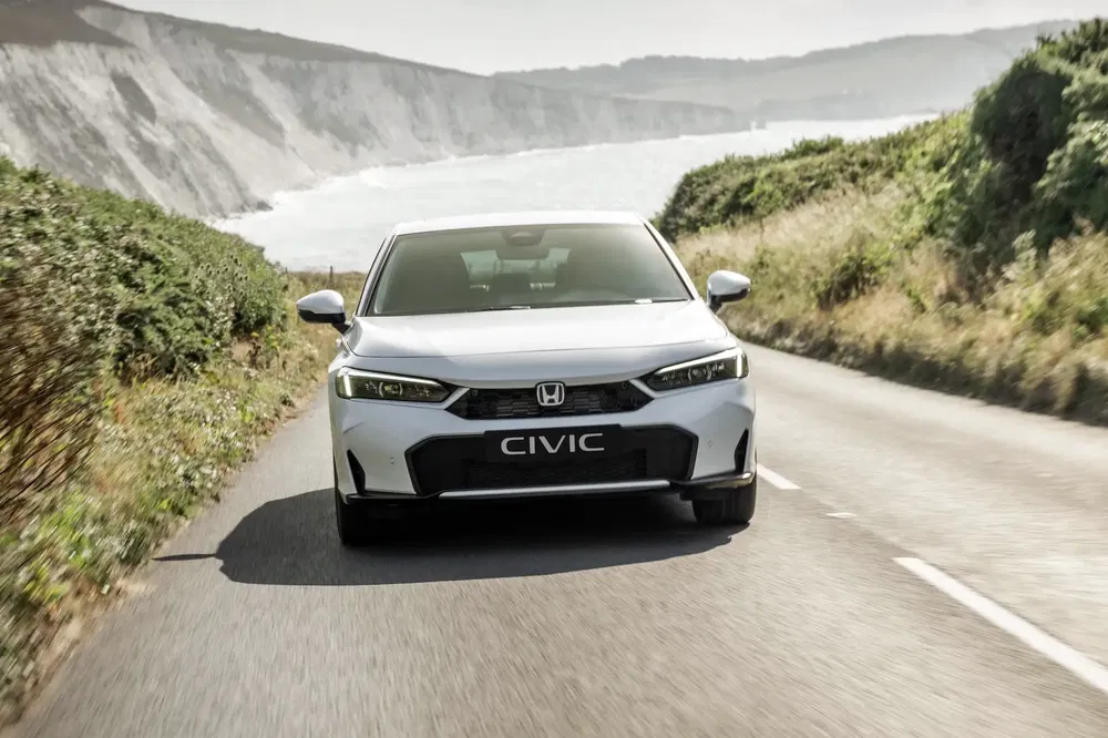 Honda Civic blanche sur route côtière bordée de végétation luxuriante.