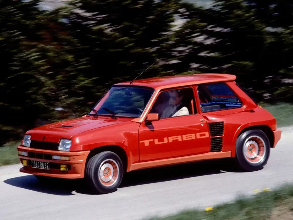 Renault 5 Turbo rouge roulant sur une route sinueuse à grande vitesse.