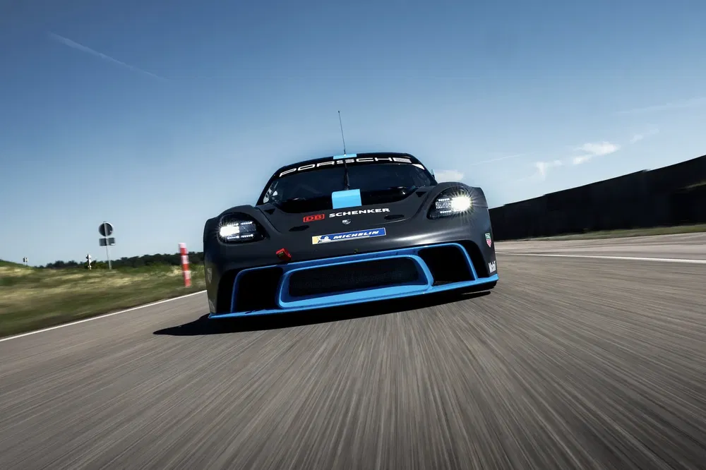 Course Porsche noire sur circuit, logo Michelin visible, ciel bleu dégagé.