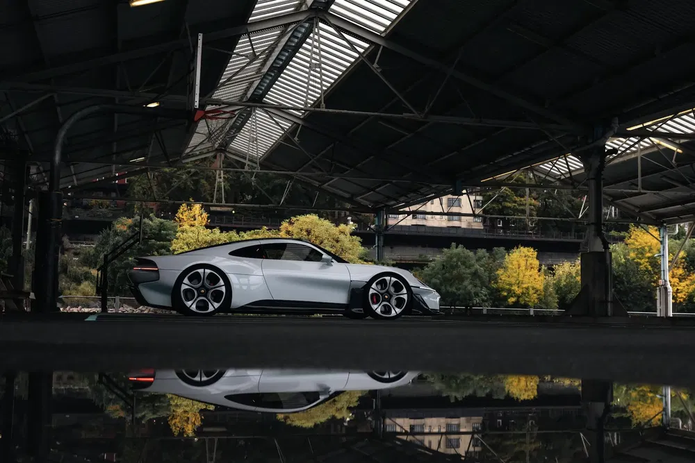 Zilveren Porsche Taycan onder overkapping, reflectie op natte grond, gele bomen op achtergrond.