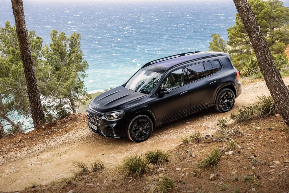 Mercedes-Benz GLC noir mat sur route côtière boisée sur fond d'océan bleu.