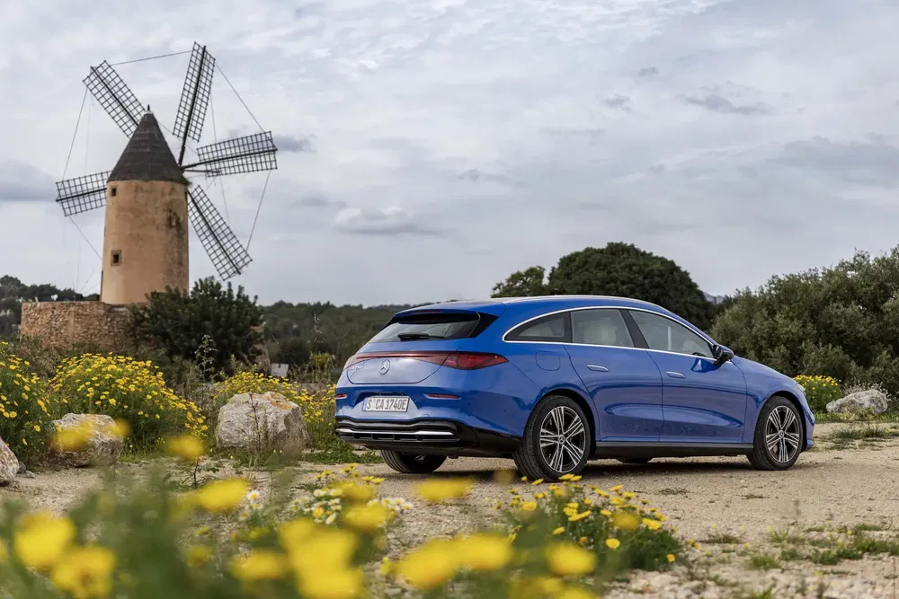 Mercedes-Benz EQE bleu près d'un moulin à vent dans un paysage champêtre.