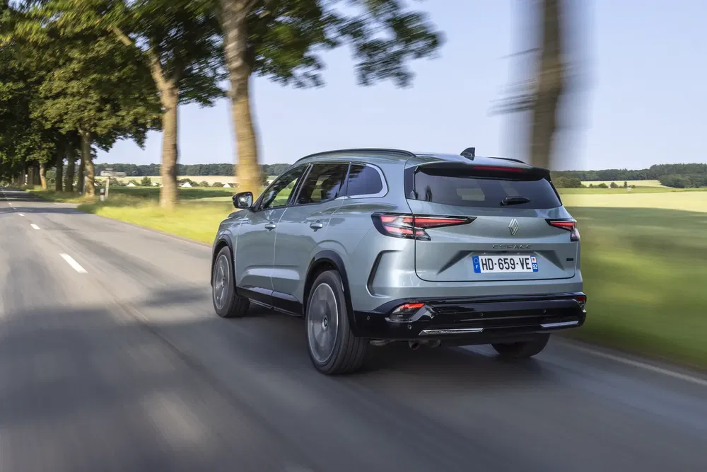 Renault Austral SUV rijdt op een met bomen omzoomde weg, blauwe lucht op de achtergrond.