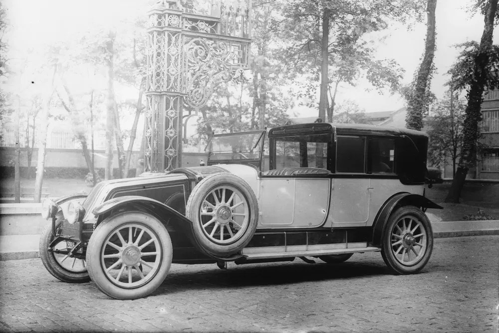 {"fr":"Voiture ancienne avec roues de secours, stationnée près d'une structure métallique ornementée.","nl":"Oude auto met reservewielen geparkeerd naast een decoratieve metalen structuur."}