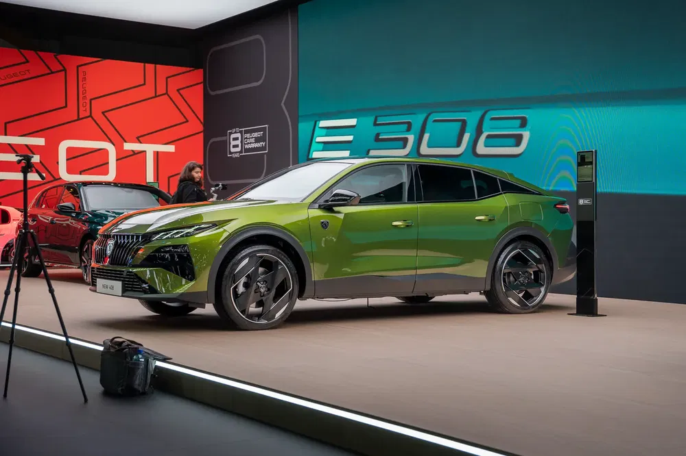 Groene Peugeot 508 op podium tijdens autobeurs, omgeven door moderne verlichting.