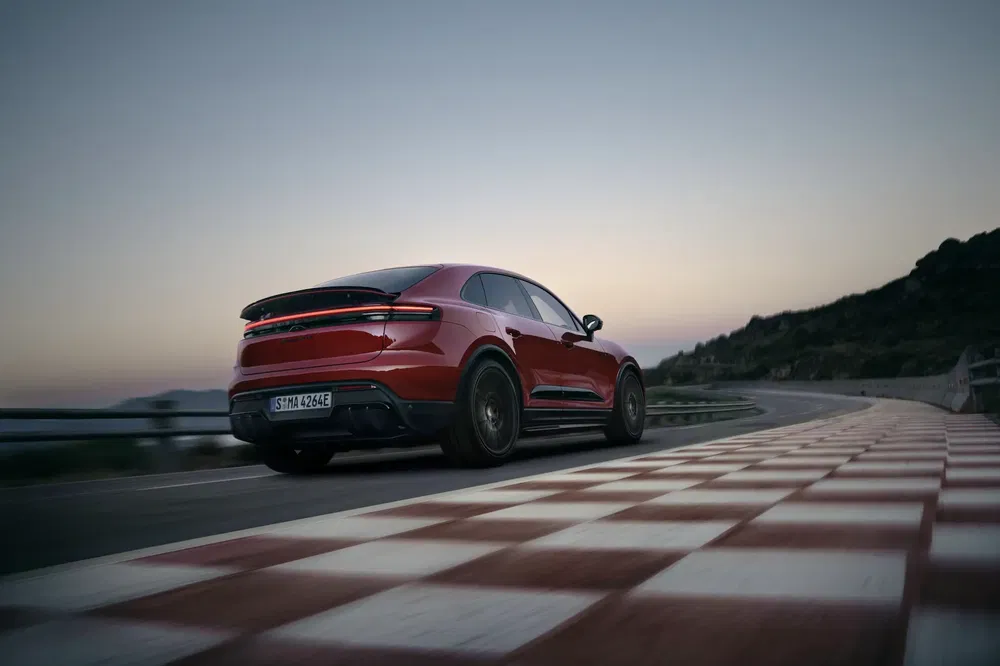 Porsche électrique rouge en mouvement sur une route sinueuse au crépuscule.