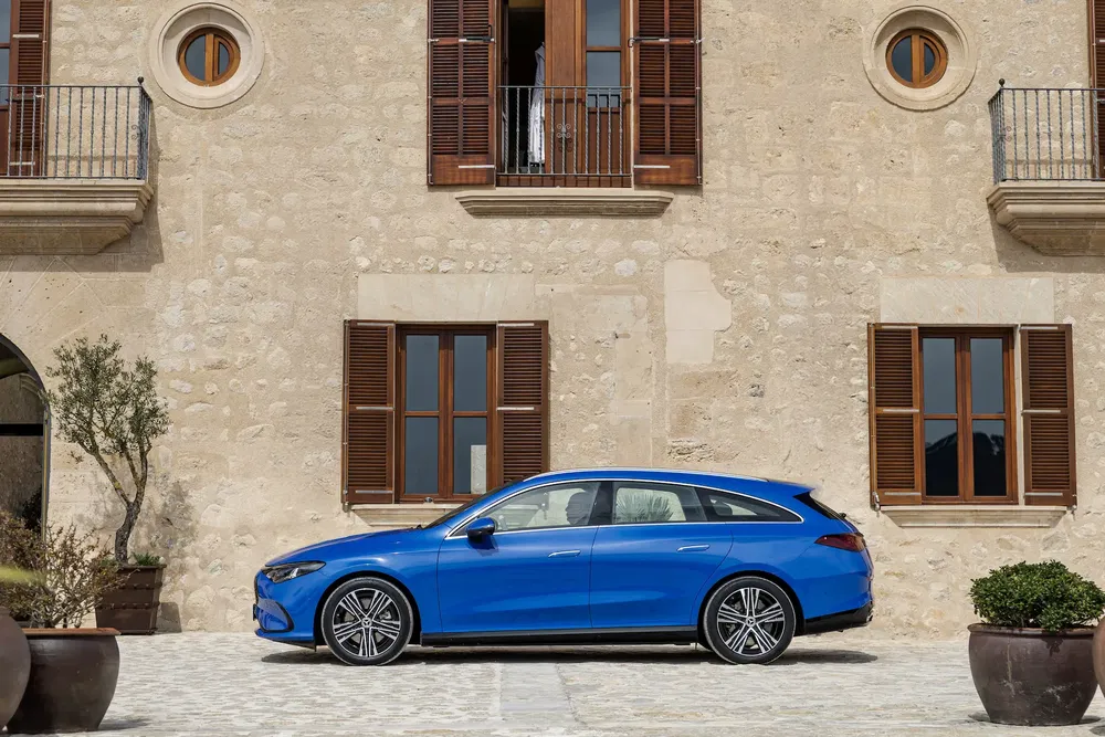 Mercedes-Benz break bleu devant un bâtiment en pierre avec fenêtres à volets en bois.