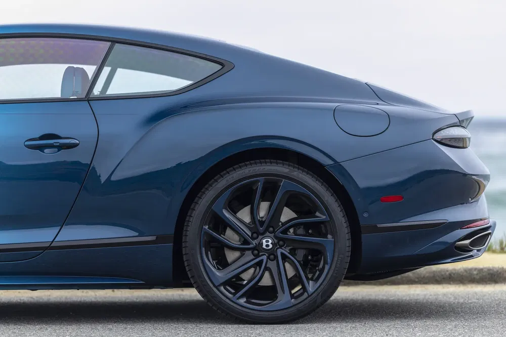 Détail arrière d'une Bentley Continental GT bleue avec jantes noires élégantes en bord de mer.