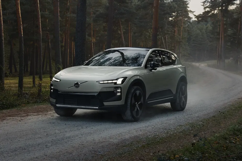 Volvo SUV gris élégant roulant sur une route forestière poussiéreuse, mélange de nature et technologie.