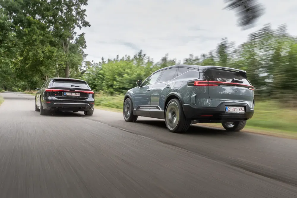 Deux voitures SUV électriques roulant rapidement sur une route de campagne bordée d'arbres.