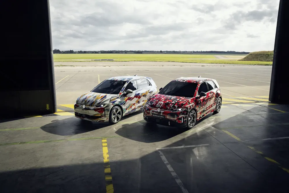 Deux voitures Volkswagen camouflées stationnées sur piste, vue aérienne, ciel nuageux à l'arrière.