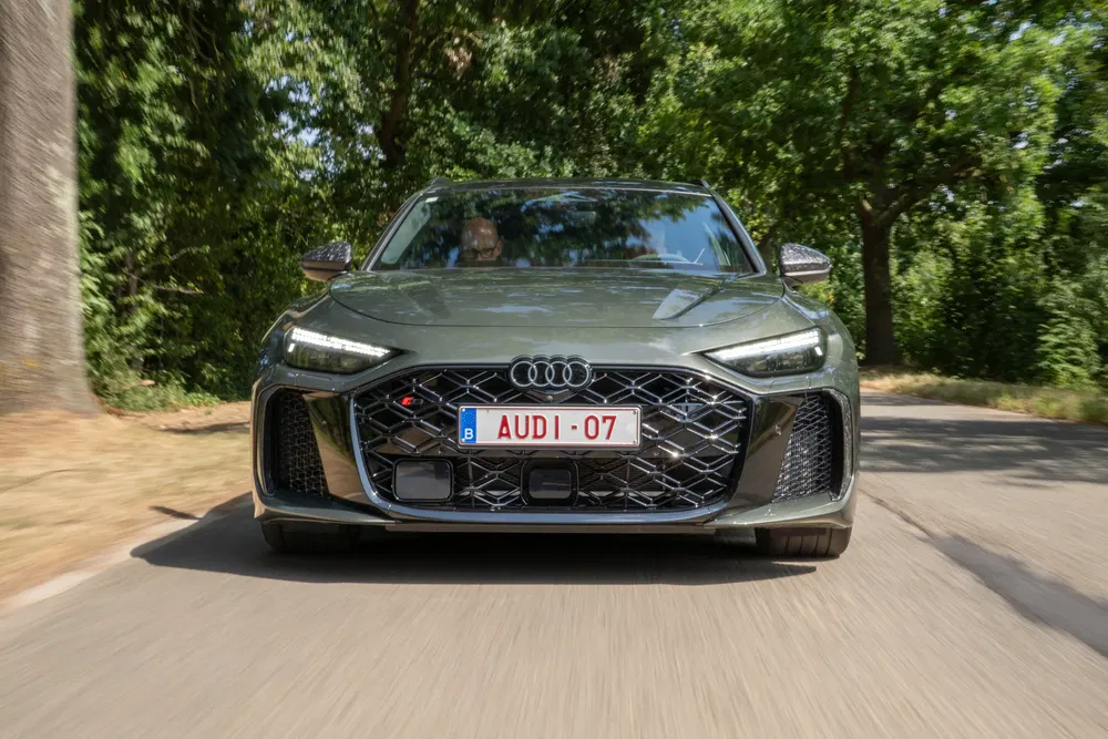Donkergroene Audi RS avant rijdend op een met bomen omzoomde weg.