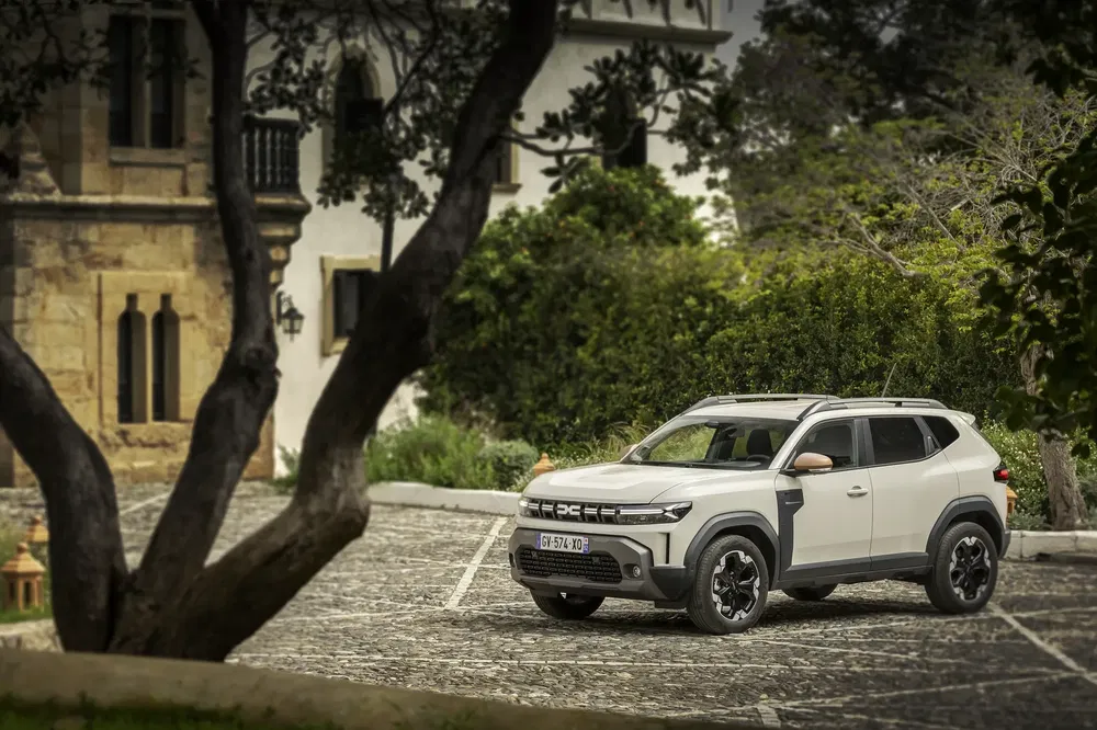 Dacia SUV geparkeerd voor een historisch huis omringd door bomen en groen.