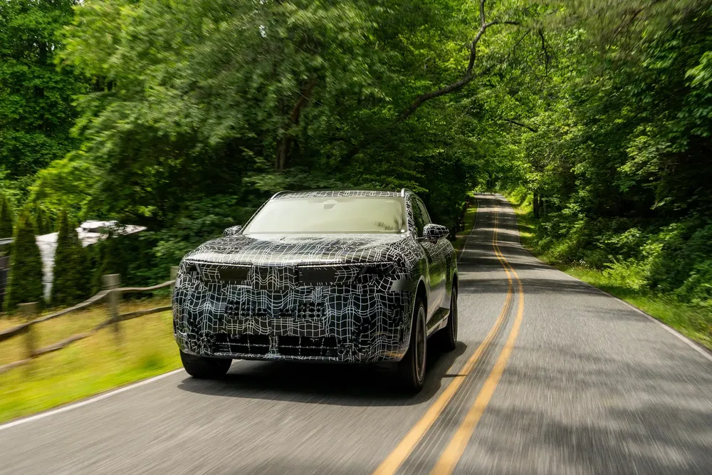 Gecamoufleerde testauto rijdend op bosrijke weg, mogelijk elektrische SUV-model.