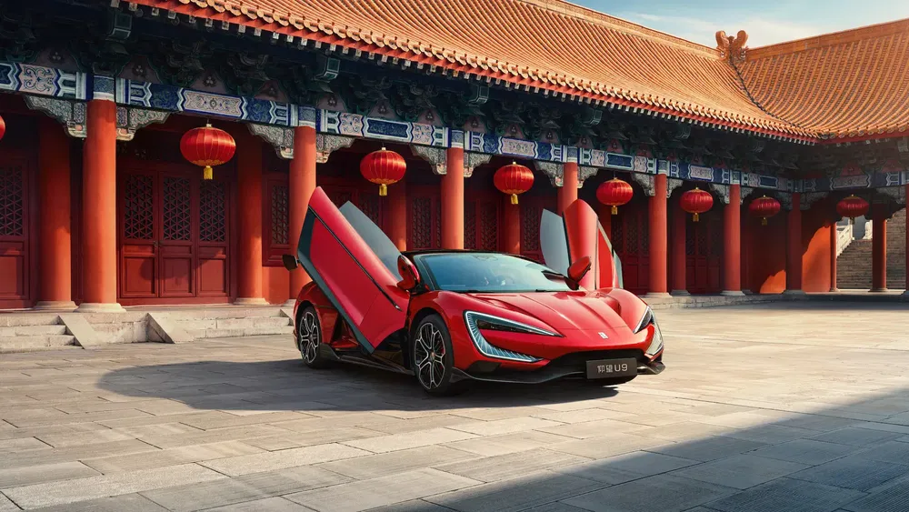 Voiture sportive BYD U9 rouge avec portes papillon devant temple traditionnel chinois.