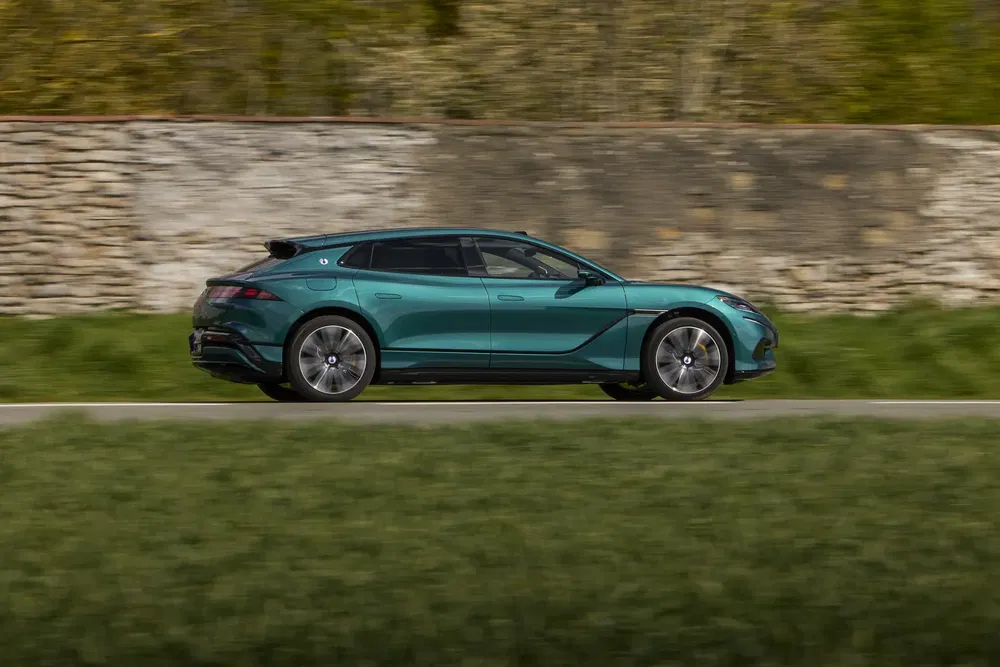 Groene Lotus Eletre elektrische auto rijdt langs stenen muur op weg.