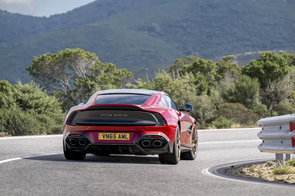 Aston Martin DB11 rouge roulant sur route de montagne sinueuse, arrière visible.